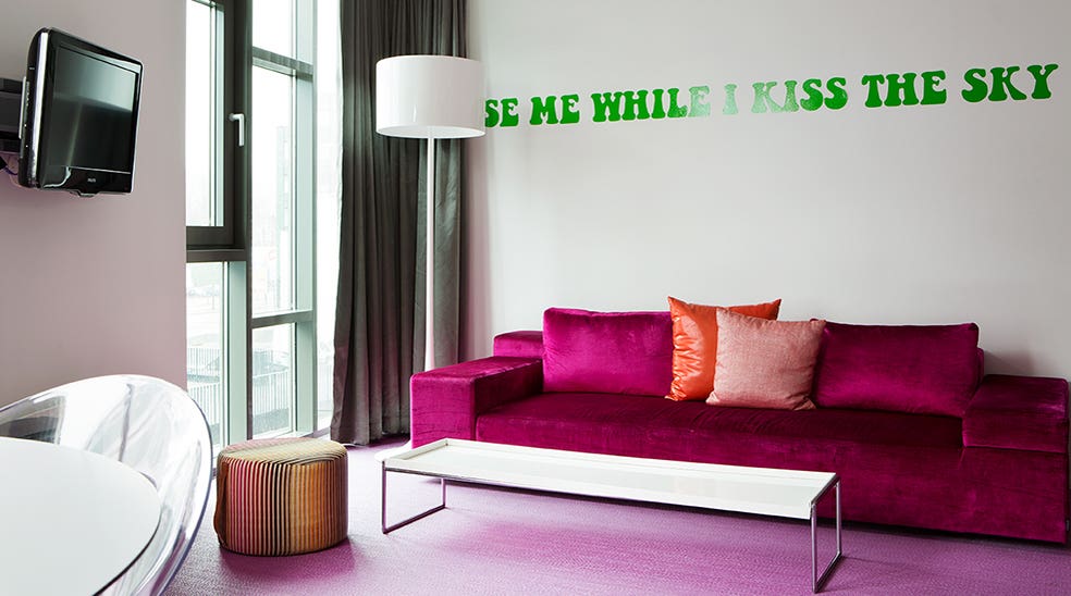 Sviten Flowerpower med rosa sammetsoffa och grön text på väggen på Comfort Hotel Union Brygge Drammen