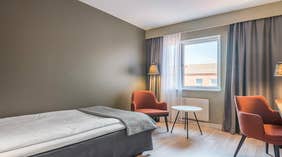 Standard enkelrum med säng, orangea stolar, fönster, lampa och bord på Quality Hotel Grand Kristianstad