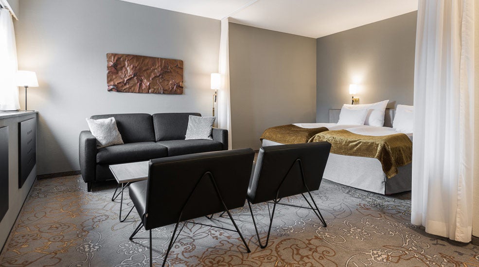 Grå soffa, dubbelsäng och svarta fåtöljer i Deluxe dubbelrum på Quality Hotel Royal Corner